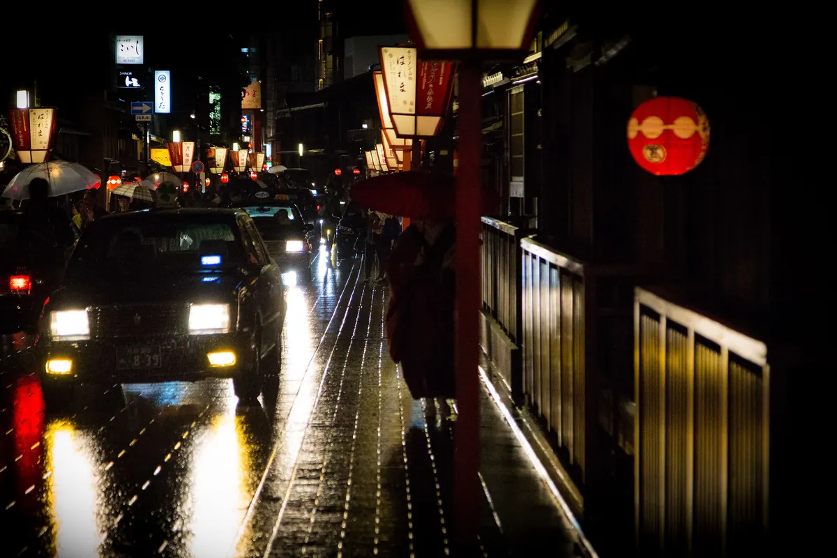 A wide paved street lined with traditional wooden townhouses in Gion, Kyoto, on a bright day