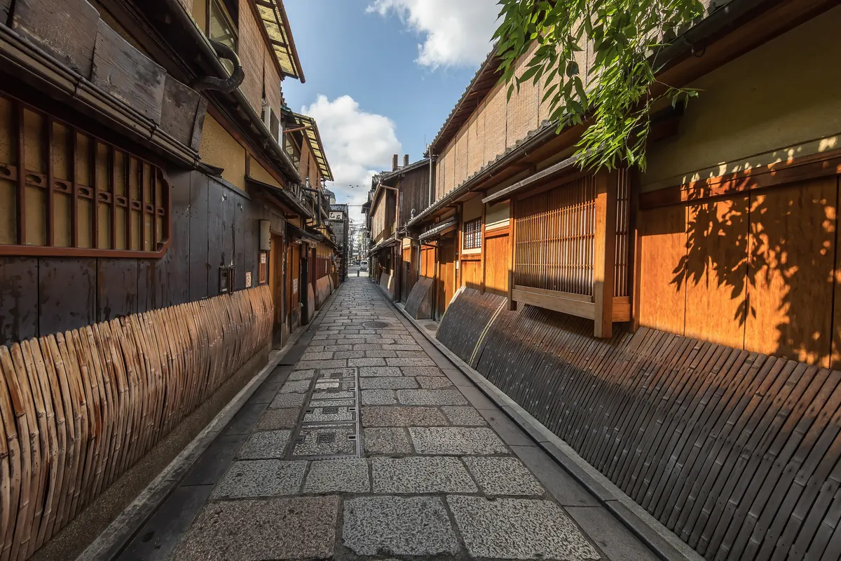 A narrow stone-paved lane in Gion between wooden facades with bamboo fences and slatted windows