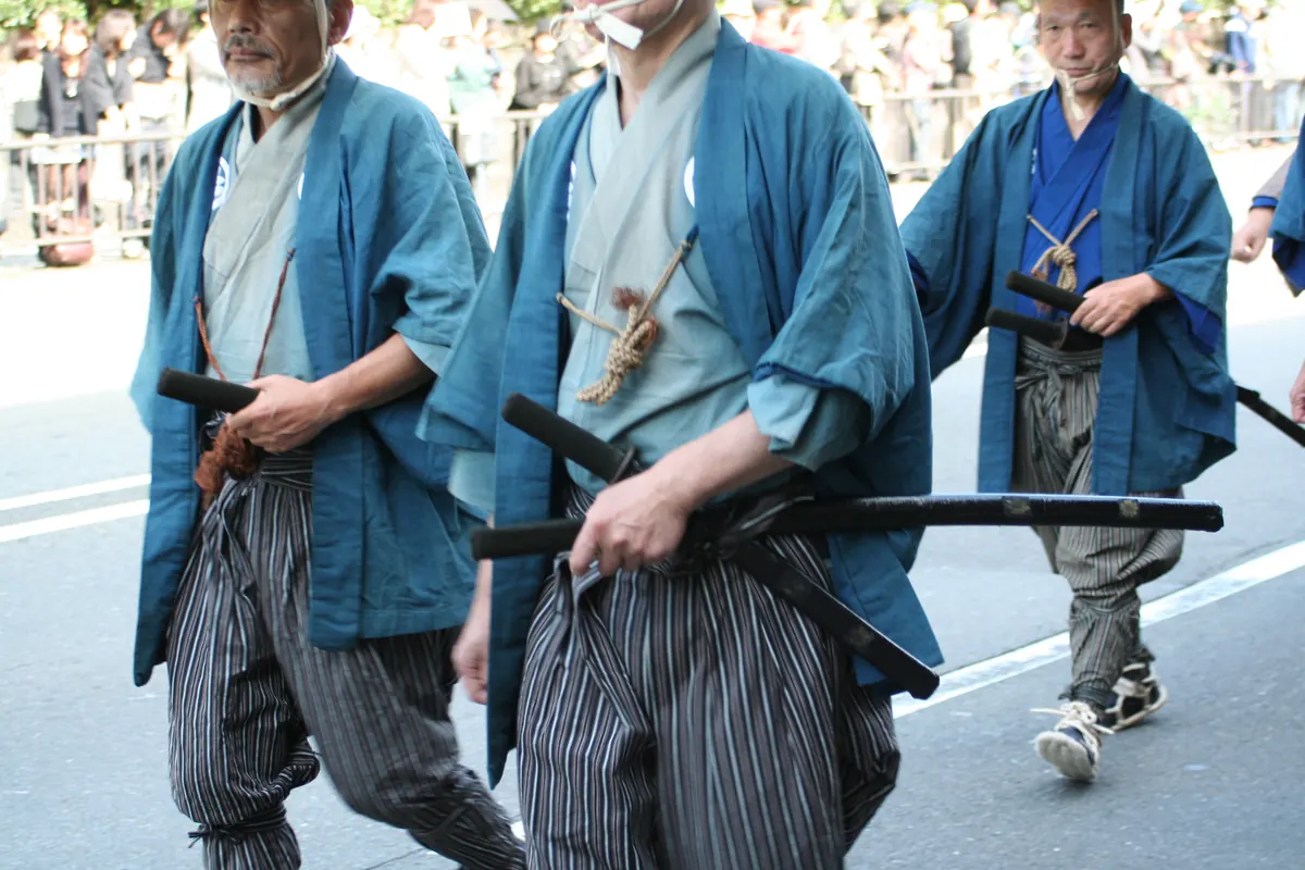 Men in samurai-era dress with swords at their belts walking in a Kyoto street procession
